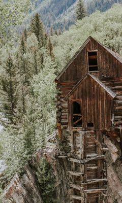 brown wooden house on rock formation near green tr... wallpaper